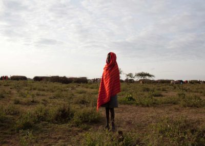 Marcy Mendelson, The Samburu Story | A Samburu boy warms himself by the light of the rising sun. Outside Kisima, Samburu County, Kenya.  August 22, 2013.