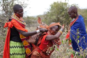 Marcy Mendelson, The Samburu Story | After hours of butchering the ritually slaughtered cows, the women pack and carry the meat in heavy sacks strapped across their head and balanced on their backs. They return to the grand manyatta to prepare the feast.