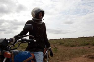 Marcy Mendelson, The Samburu Story | A dash of modernity as a young Samburu man runs errands to the village of Kisima for cell phone minutes and cigarettes during the Lmuget ceremony. Outside Kisima, Samburu County, Kenya. August 22, 2013.